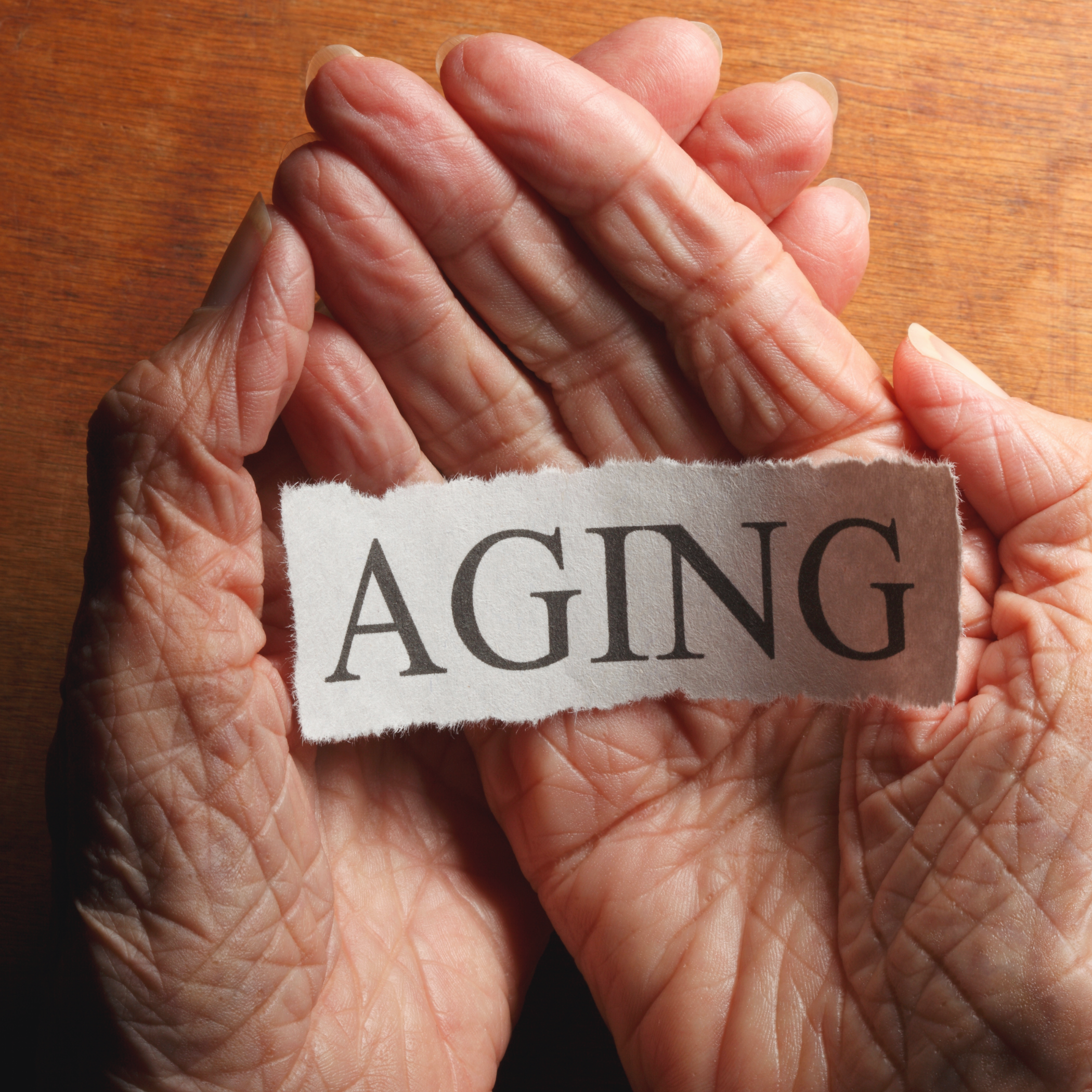 Close‑up of older hands gently holding a paper strip with the word ‘aging’, symbolising how NAD+ and ageing research looks at the biology behind growing older.